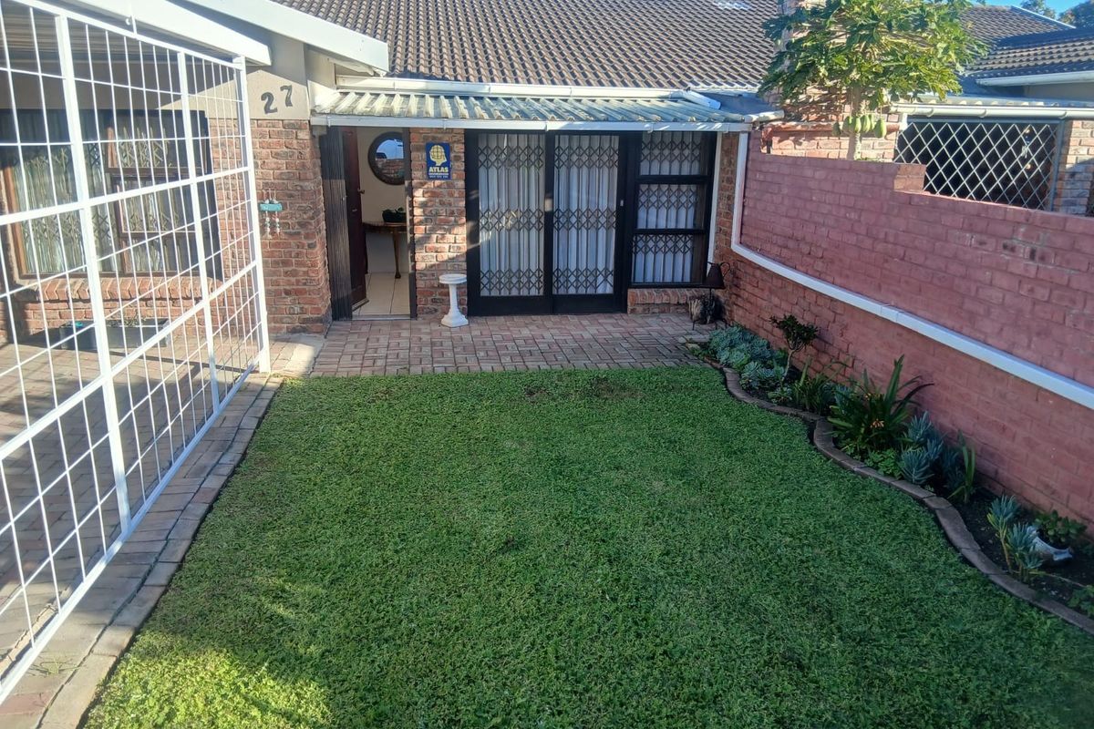 A private rear courtyard featuring a paved patio area, a small lawn, and a brick boundary wall with established garden beds.