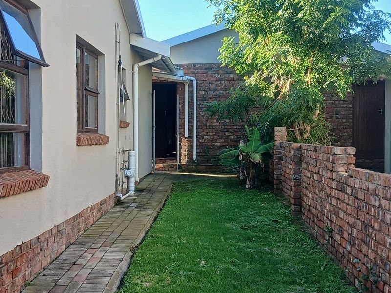 A side exterior view of the townhouse featuring a paved walkway, a small lawn area, and a brick boundary wall.
