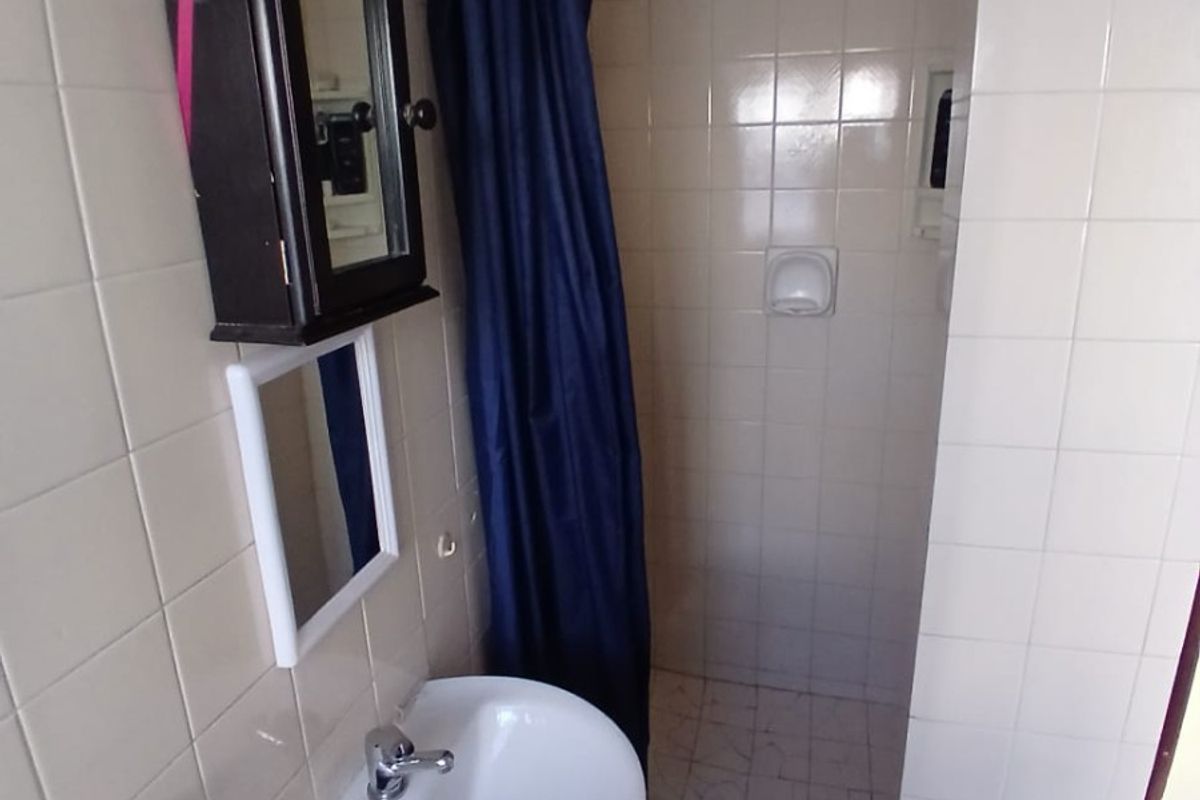 A compact bathroom featuring a pedestal basin, tiled walls, and a shower enclosure with a curtain.