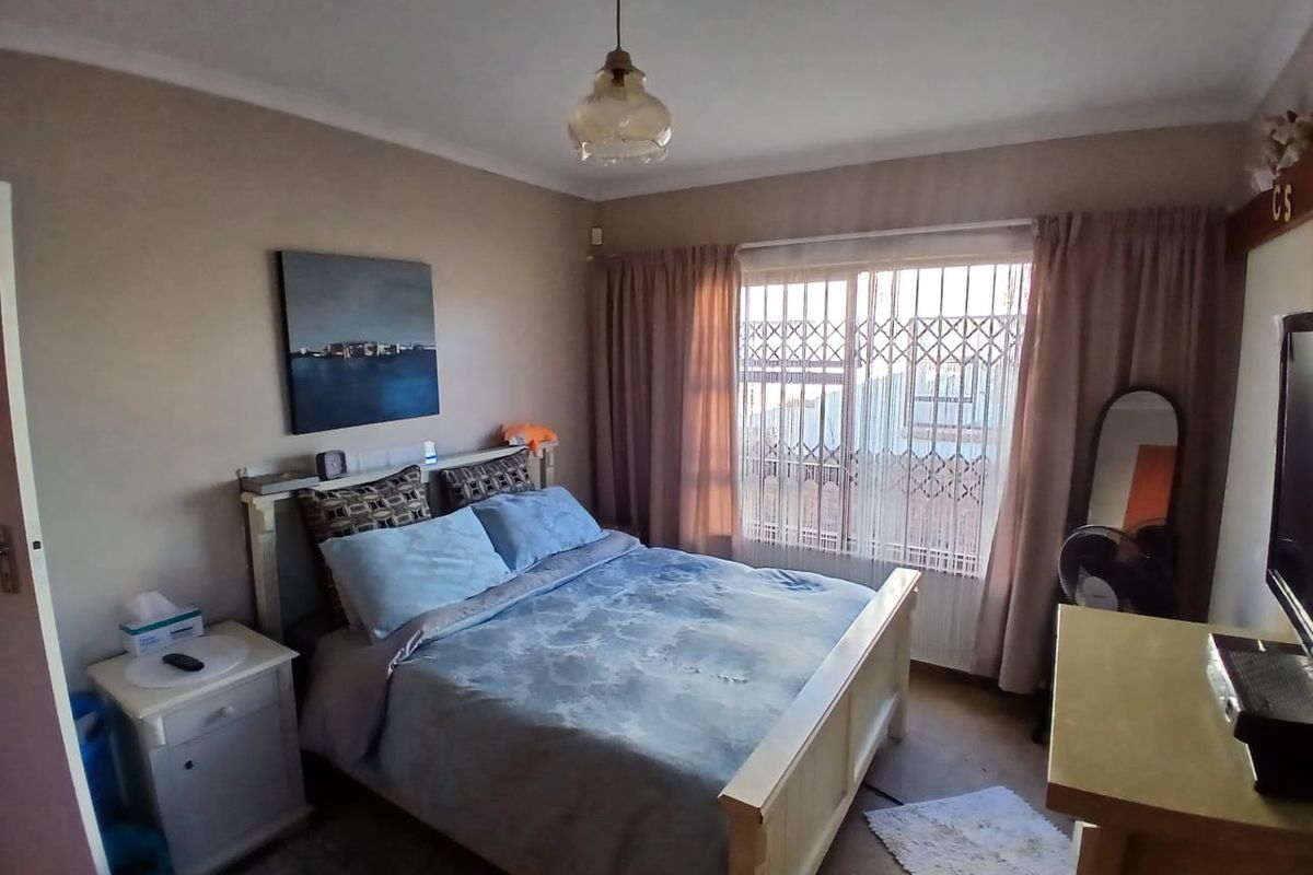 A standard bedroom featuring a large window with security bars, neutral wall tones, and carpeted flooring.