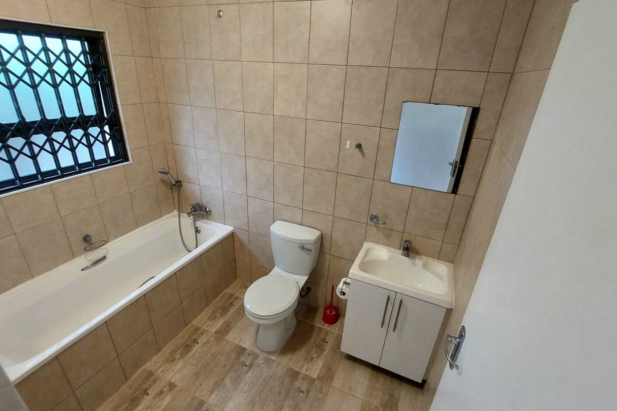 A functional bathroom featuring a bathtub with shower mixer, a vanity basin, and a toilet, finished with neutral wall tiles and wood-look flooring.