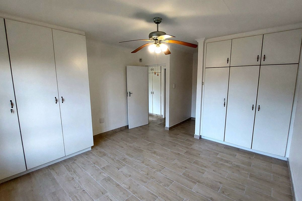A bright bedroom featuring extensive built-in cabinetry, wood-look tiled flooring, and a central ceiling fan.