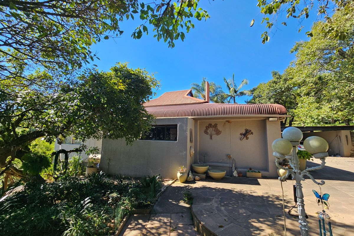 A view of the rear exterior of the house featuring a covered patio area, paved courtyard, and established garden surroundings.