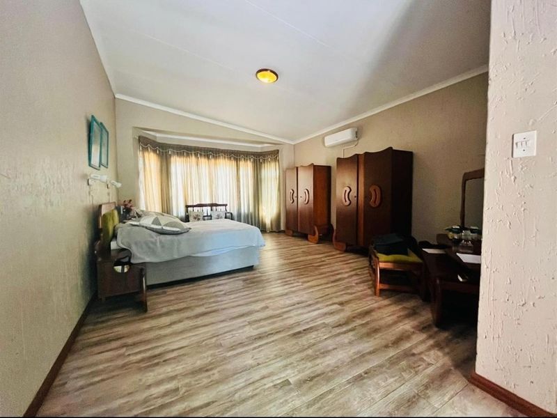 Spacious bedroom featuring wood-look laminate flooring, a large bay window with curtains, and a wall-mounted air conditioning unit.