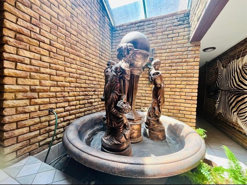 An indoor courtyard area featuring a decorative water fountain, exposed brick walls, and a skylight providing natural illumination.