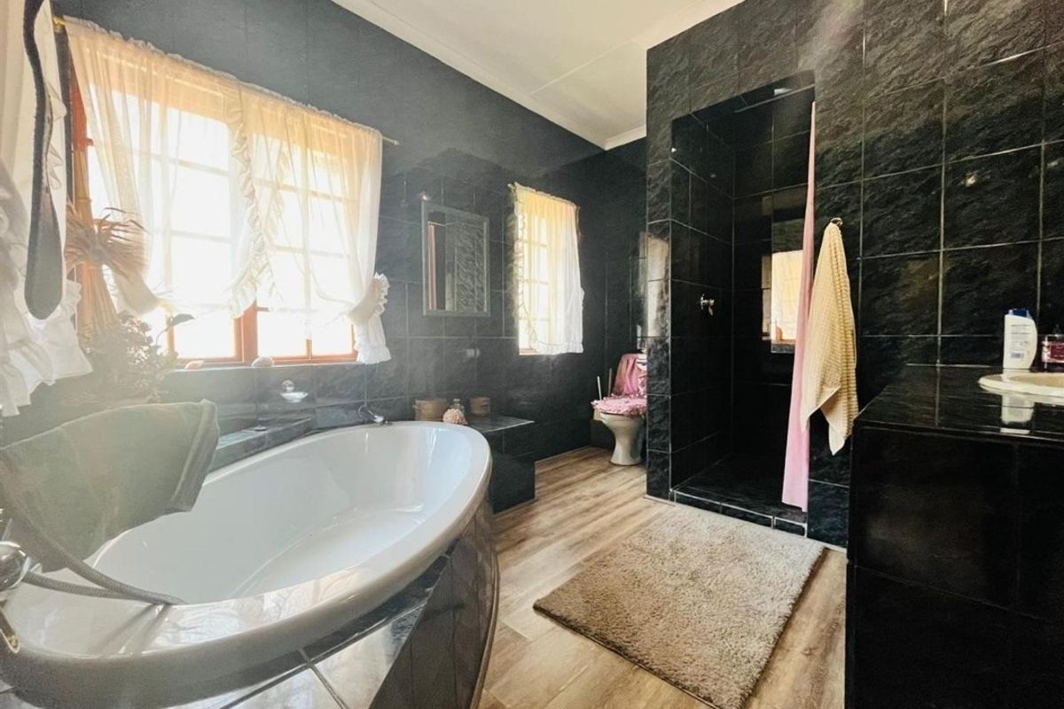 Spacious bathroom featuring a large soaking tub, a walk-in shower enclosure with dark tiling, and wood-look flooring.
