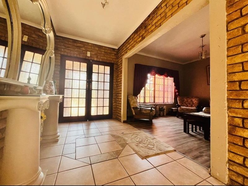 An open-plan living area featuring exposed brick walls, tiled flooring, and double glass-paned entrance doors, creating a warm and traditional atmosphere.