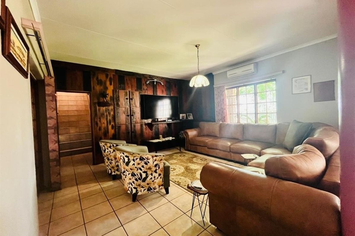 A spacious living room featuring tiled flooring, a wood-paneled feature wall, and a wall-mounted air conditioning unit.