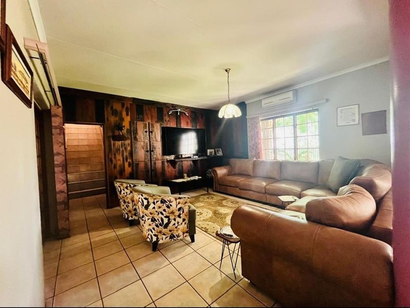 A spacious living room featuring tiled flooring, a wood-paneled feature wall, and a wall-mounted air conditioning unit.