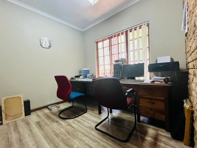 A functional home office space featuring wood-look laminate flooring, a large window with vertical blinds, and a textured brick feature wall.