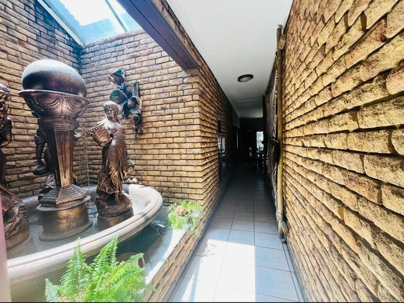 A unique indoor hallway featuring exposed brick walls, tiled flooring, and a built-in water feature with a skylight above.