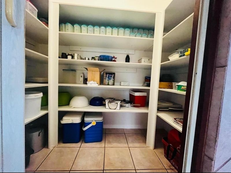 A functional walk-in pantry featuring built-in white shelving units and tiled flooring, providing ample storage space for kitchen essentials.