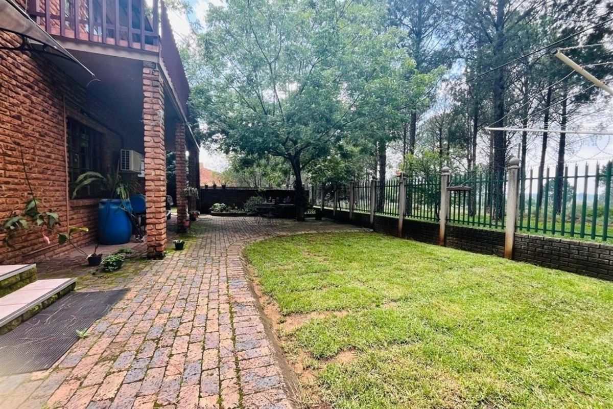 A private rear garden featuring a brick-paved patio area, established lawn, and secure perimeter fencing with mature trees in the background.