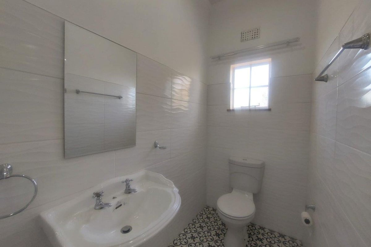 A clean, modern bathroom featuring a pedestal basin, wall-mounted mirror, toilet, and decorative patterned floor tiles with white wall tiling.