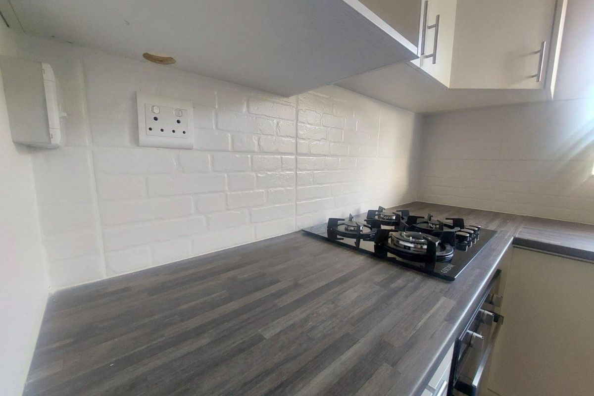 A modern kitchen workspace featuring dark wood-look laminate countertops, a built-in gas hob, and white subway-style tiled splashbacks with overhead cabinetry.