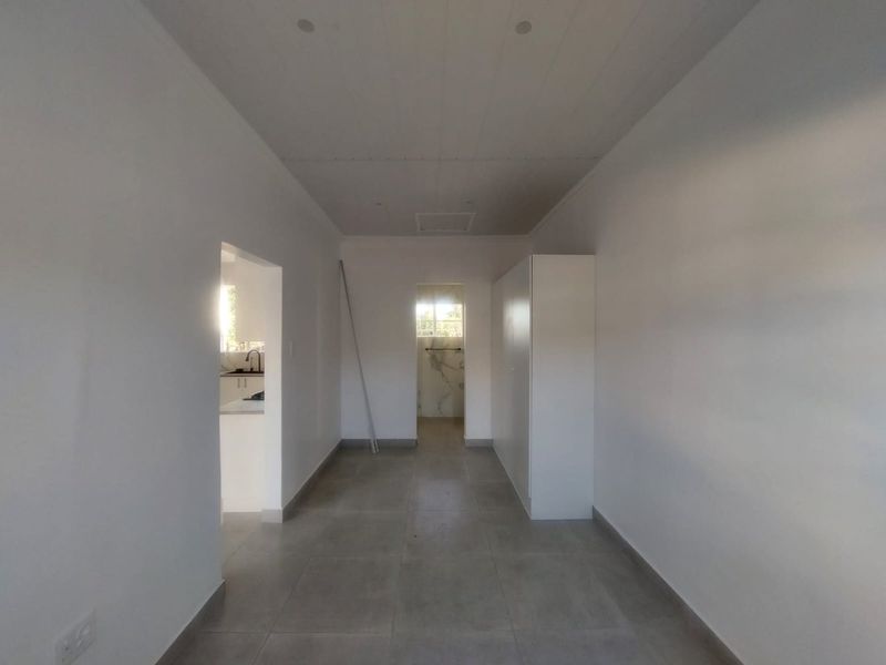 A bright, neutral hallway featuring large-format floor tiles, recessed ceiling lighting, and built-in cabinetry, providing a clean and modern transition between living spaces.