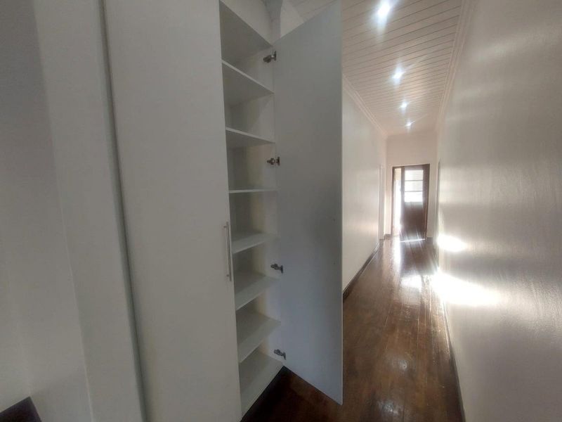 A bright hallway featuring polished timber flooring, recessed ceiling lighting, and a built-in floor-to-ceiling storage cupboard with white cabinetry.
