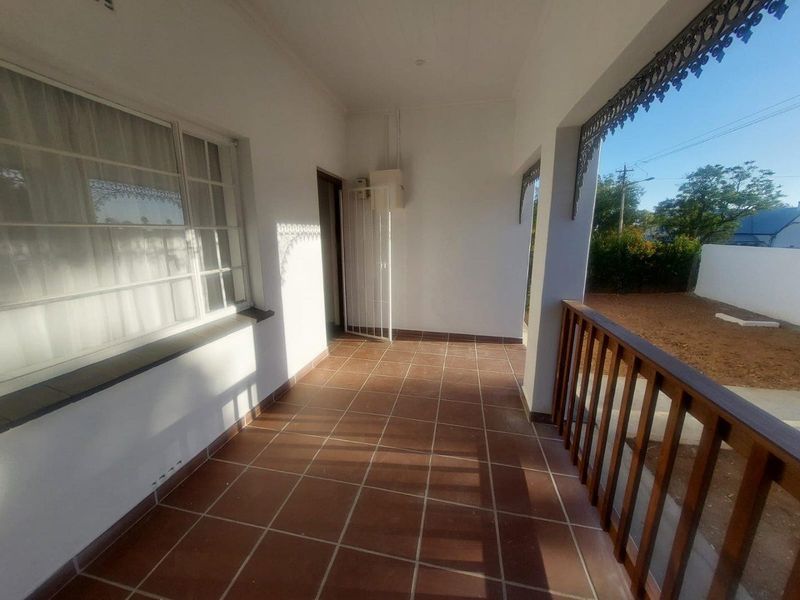 A covered patio area featuring tiled flooring, decorative metal trim, and a timber railing overlooking the side garden.