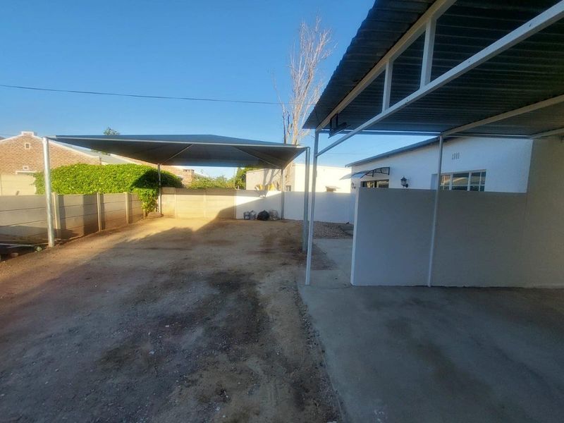 Outdoor area featuring a covered carport structure and a shade sail, providing sheltered parking space within a fenced property boundary.