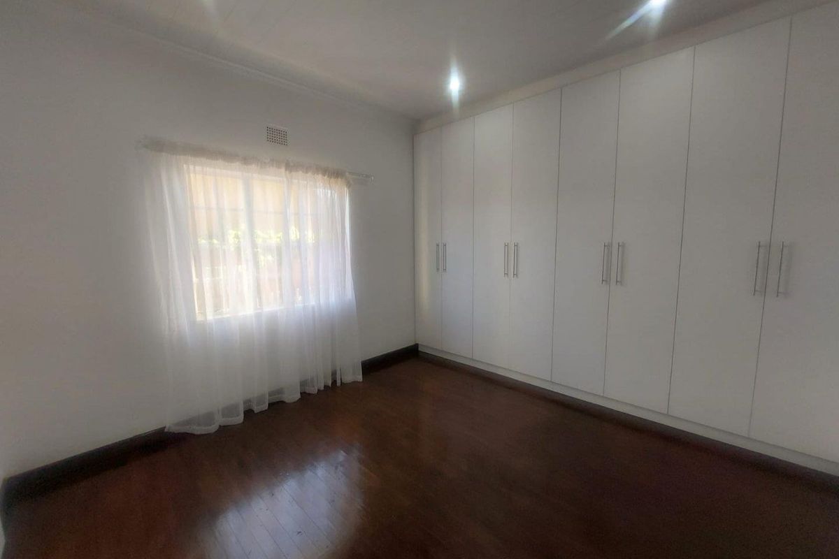 A bright bedroom featuring polished timber flooring and extensive floor-to-ceiling built-in cabinetry with modern white finishes.