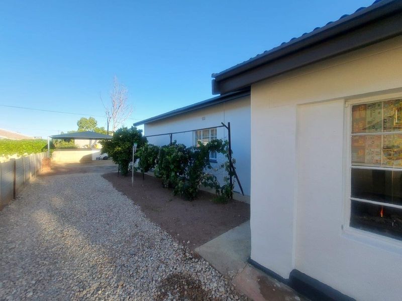 Side exterior view of the property featuring a gravel driveway, white painted exterior walls, and a metal trellis structure.