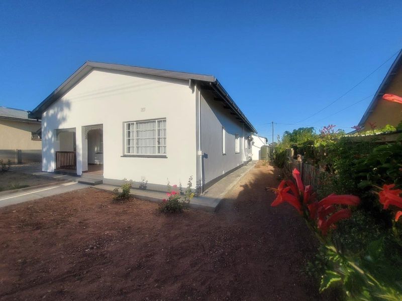 Exterior view of the house featuring a white facade, covered front porch, and surrounding garden area with a gravel path.