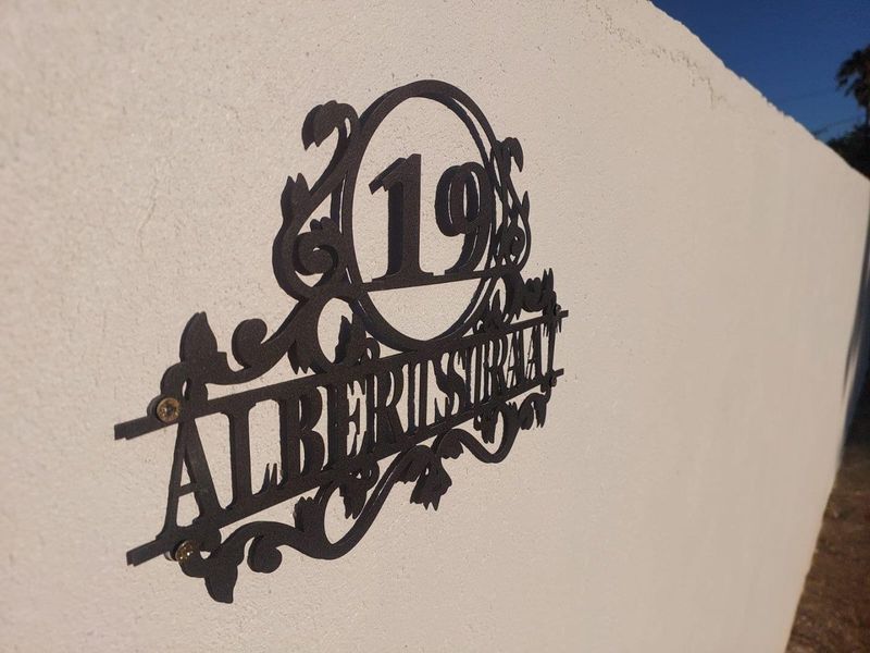 A decorative metal house number plaque mounted on a rendered boundary wall.