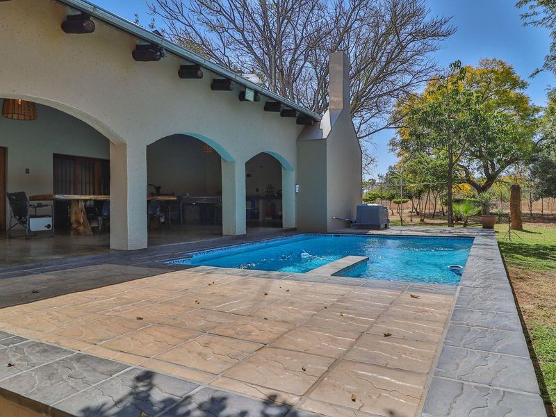 Spacious covered patio area featuring arched architectural details, overlooking a private swimming pool and well-maintained garden setting.