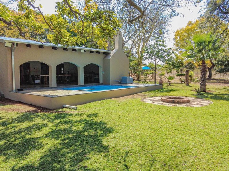 Spacious covered patio area featuring arched openings, overlooking a swimming pool and a landscaped garden with a built-in fire pit.