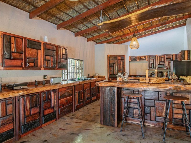 Rustic kitchen featuring custom handcrafted wooden cabinetry, a live-edge timber breakfast bar, exposed thatch ceiling beams, and polished concrete flooring.