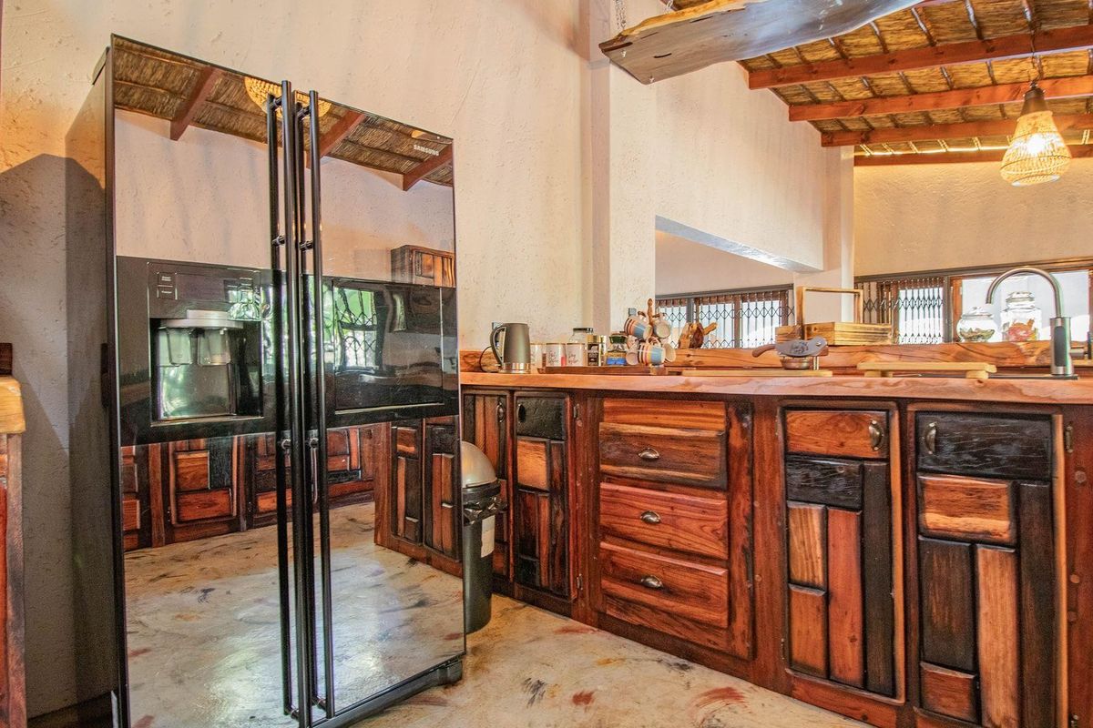 Rustic kitchen featuring custom dark wood cabinetry, a large mirrored refrigerator, and a unique exposed thatch ceiling with wooden beams.