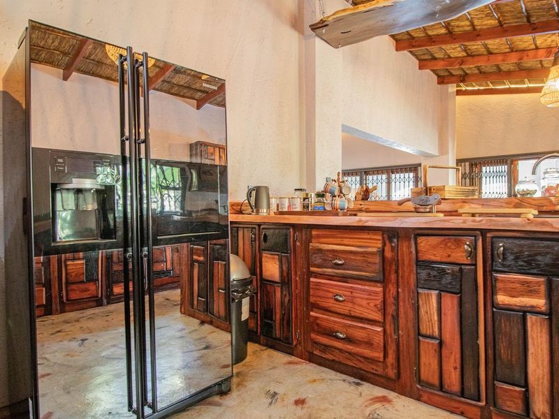 Rustic kitchen featuring custom dark wood cabinetry, a large mirrored refrigerator, and a unique exposed thatch ceiling with wooden beams.