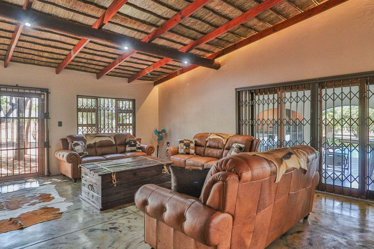 Spacious living area featuring a rustic exposed thatch roof with timber beams, polished concrete flooring, and large sliding doors with security gates.