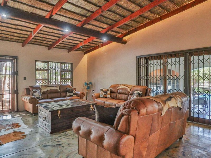 Spacious living area featuring a rustic exposed thatch roof with timber beams, polished concrete flooring, and large sliding doors with security gates.