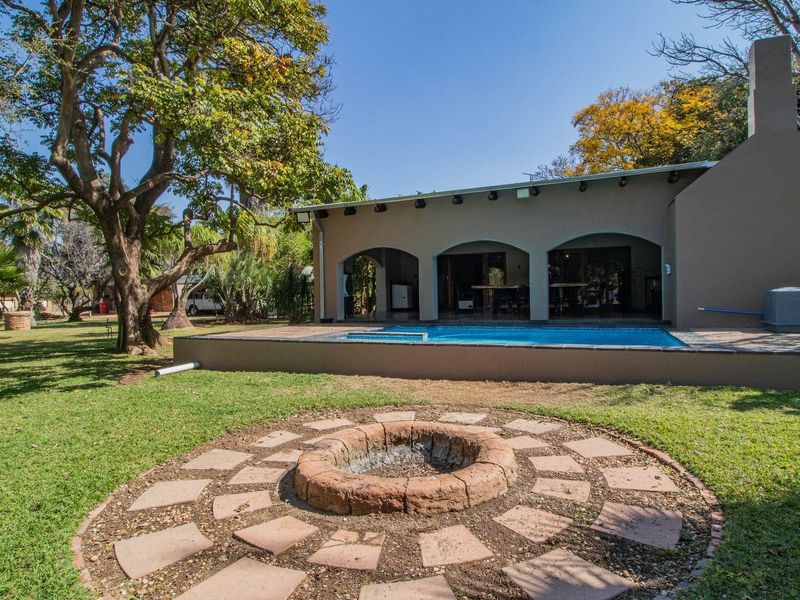 A spacious rear garden featuring a swimming pool, a covered patio area, and a circular stone fire pit set within a well-maintained lawn.