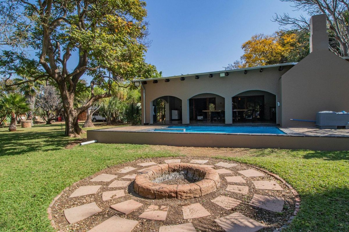 A spacious rear garden featuring a swimming pool, a covered patio area, and a circular stone fire pit set within a well-maintained lawn.