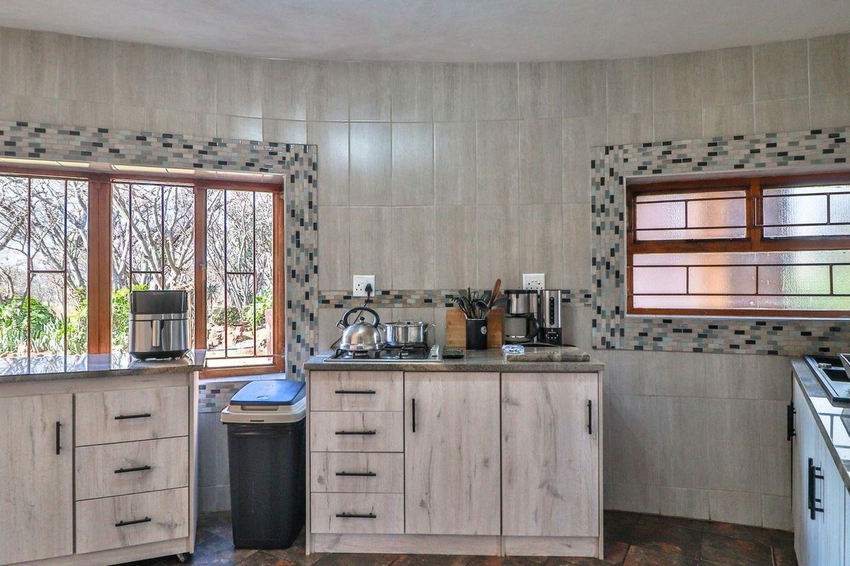 A functional kitchen area featuring light wood-grain cabinetry, stone-look countertops, tiled splashbacks, and security bars on the windows.