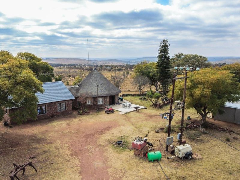 Aerial view of a farm property featuring a traditional thatched-roof dwelling, metal-roofed outbuildings, and expansive surrounding landscape.