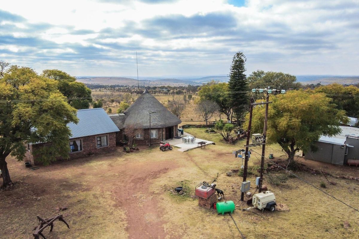 Aerial view of a farm property featuring a traditional thatched-roof dwelling, metal-roofed outbuildings, and expansive surrounding landscape.