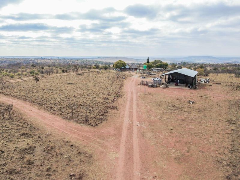 Aerial view of a rural farm property featuring a large open-sided metal shed, dirt access roads, and expansive surrounding landscape.