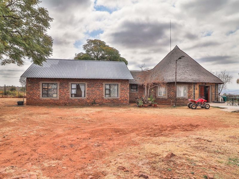 A rustic farm-style dwelling featuring a combination of corrugated metal and traditional thatched roofing, set on a large open plot.