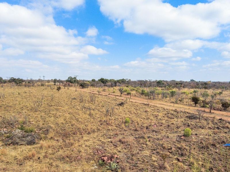 An expansive aerial view of the farm landscape, featuring natural veld, dirt access tracks, and open terrain under a clear blue sky.