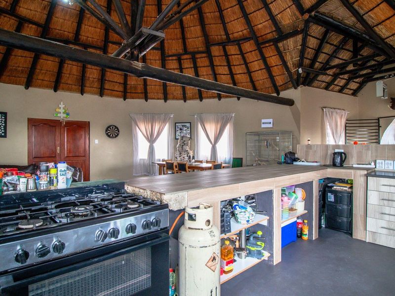 Open-plan kitchen and living area featuring a traditional thatched roof, exposed timber beams, and a built-in gas stove with a large breakfast counter.