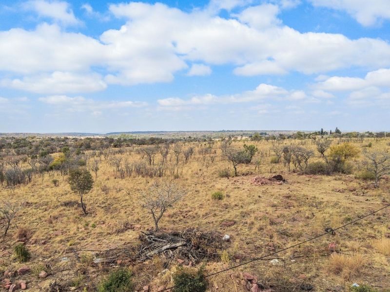 Expansive view of the open farm landscape featuring natural vegetation and a concrete water reservoir in the foreground.