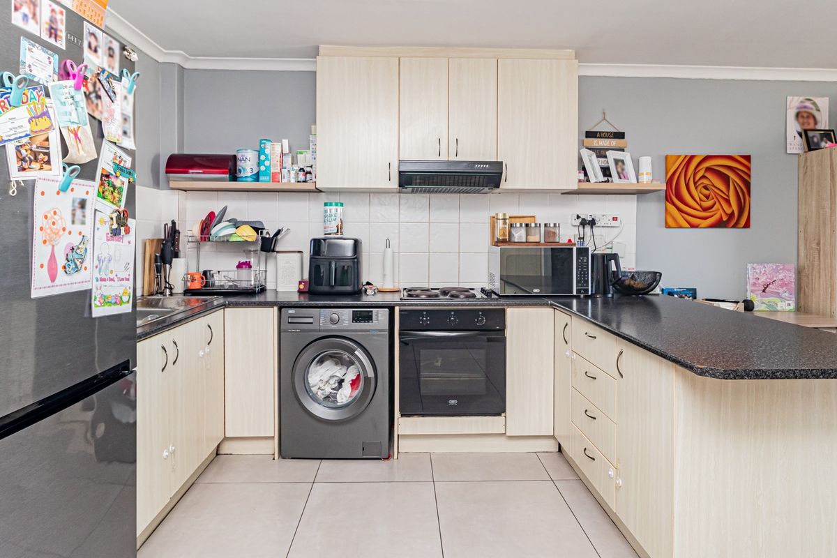 A functional kitchen featuring light wood cabinetry, dark countertops, a built-in oven, hob, extractor fan, and an integrated washing machine.