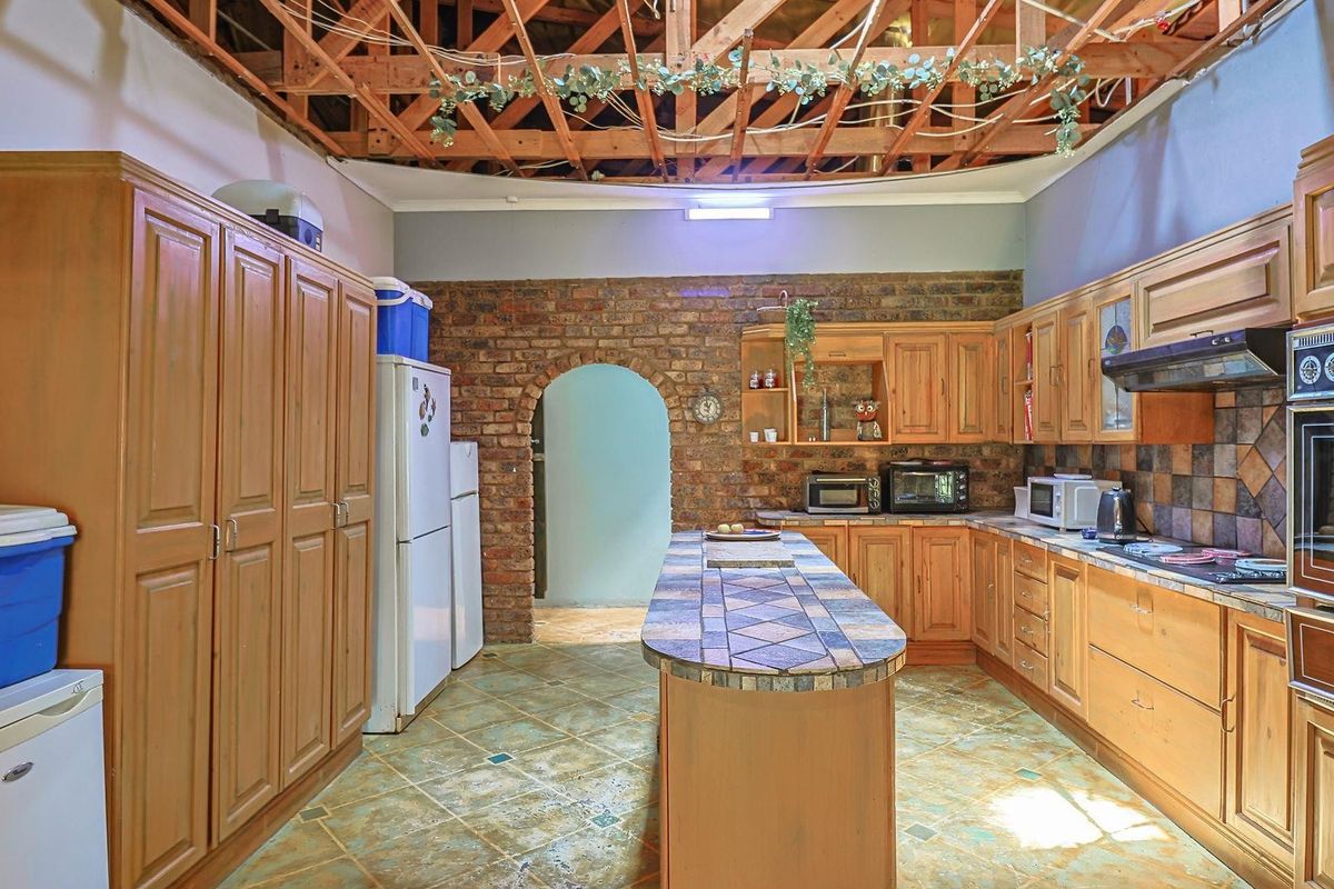 Rustic kitchen featuring wooden cabinetry, a tiled island, exposed brick wall with arched doorway, and exposed timber roof trusses.