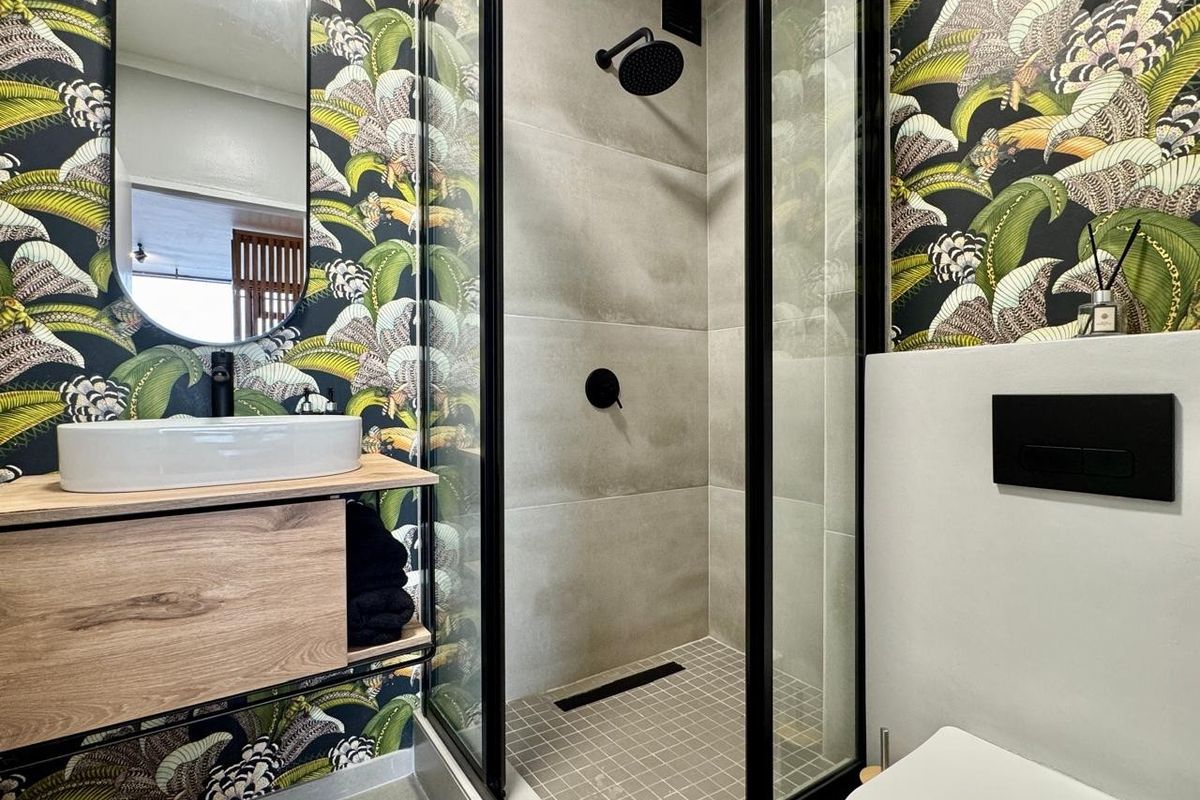 Modern bathroom featuring a walk-in shower with black fixtures, a floating vanity with a vessel sink, and bold botanical wallpaper.