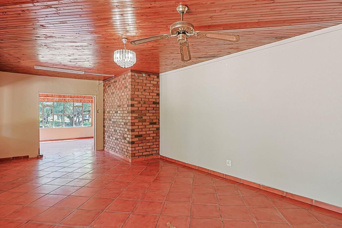 Spacious living area featuring a rustic brick feature wall, terracotta tiled flooring, and a timber-clad ceiling with a central fan.