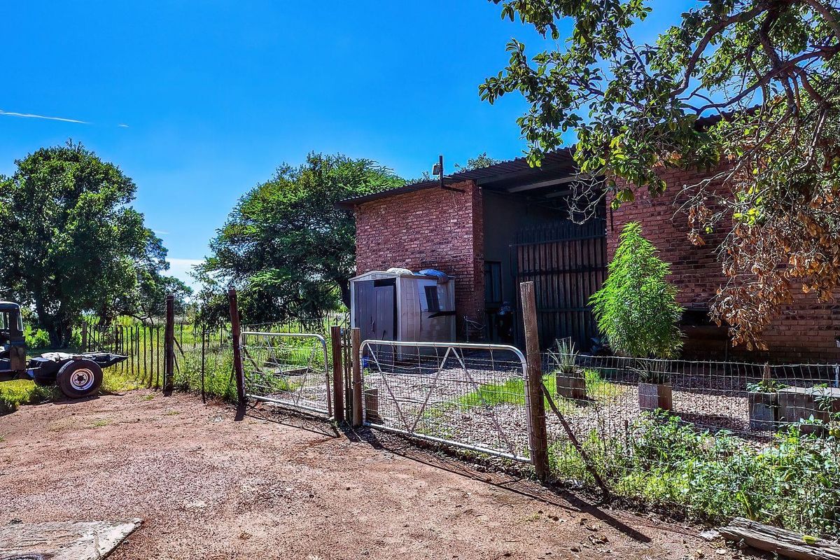 Exterior view of a rustic farm building featuring exposed brick construction, metal sliding doors, and a fenced yard area on a rural property.
