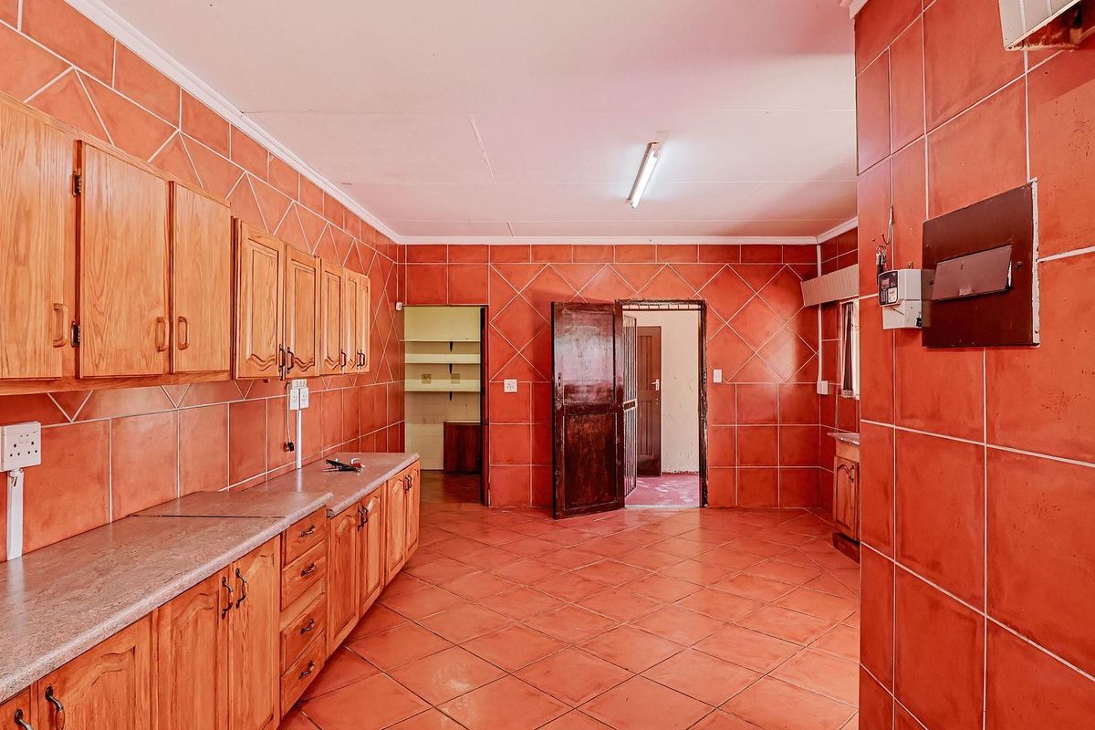 A spacious kitchen featuring extensive wooden cabinetry, tiled walls and flooring, and a functional layout with an adjacent pantry or utility area.